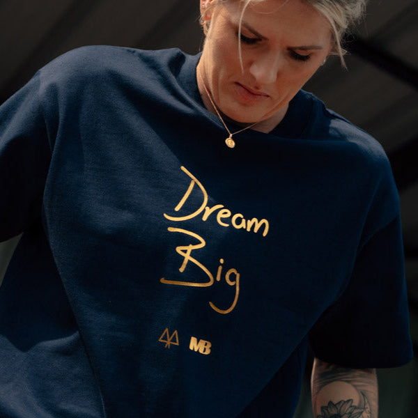 Millie Bright wearing a navy blue t-shirt with 'Dream Big' in gold text.