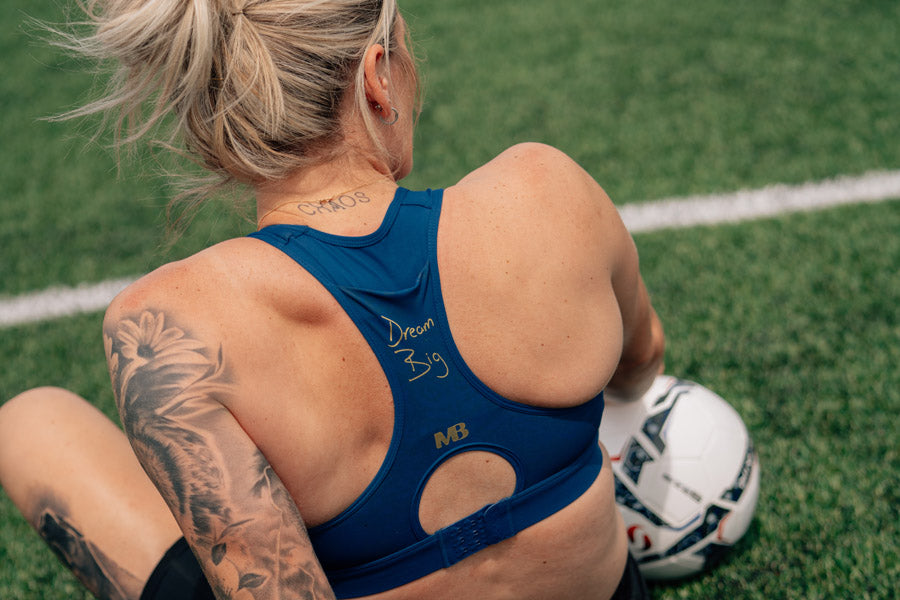 Person wearing a blue sports bra with tattoos on a grassy field