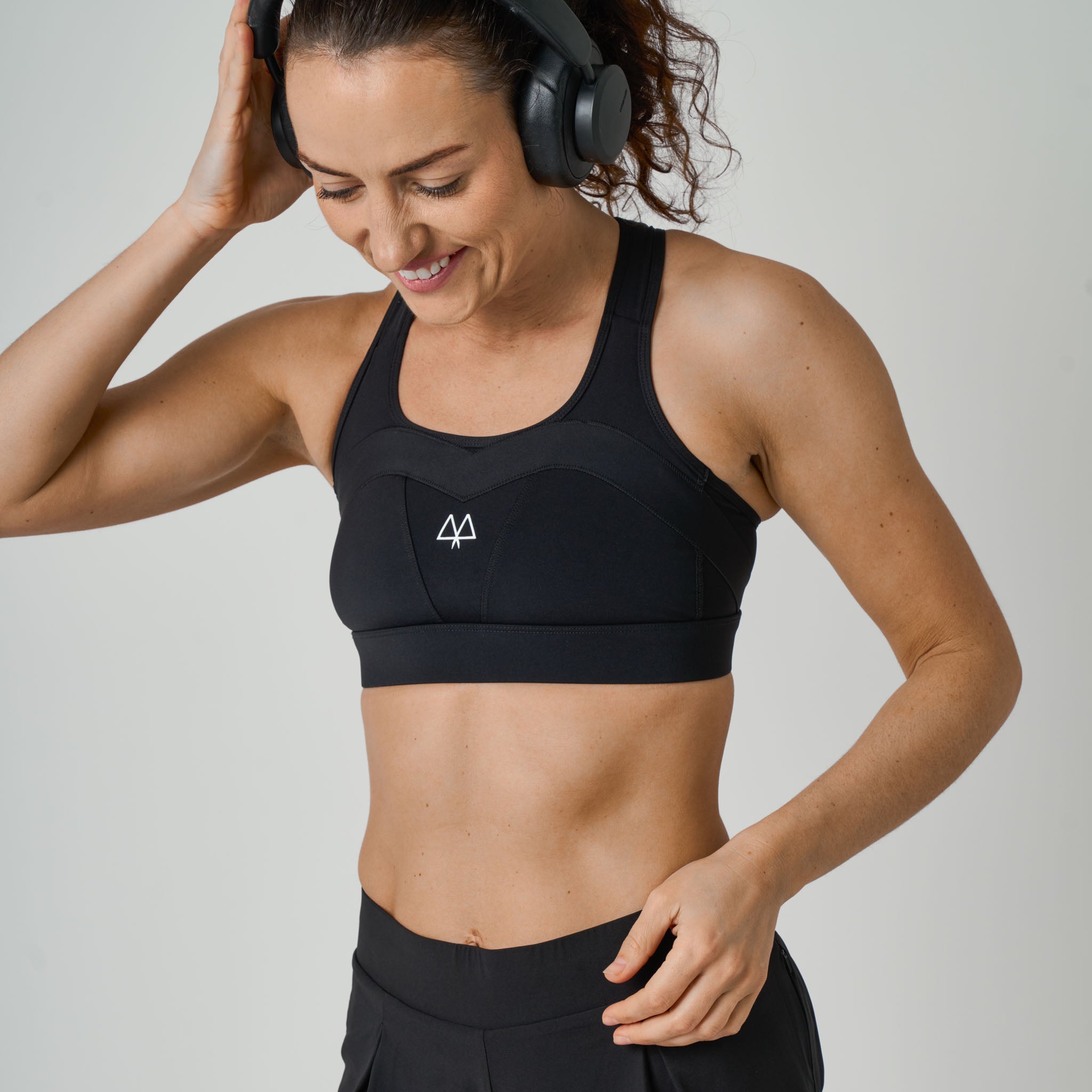 Woman wearing a black sports bra and leggings with headphones on a light gray background