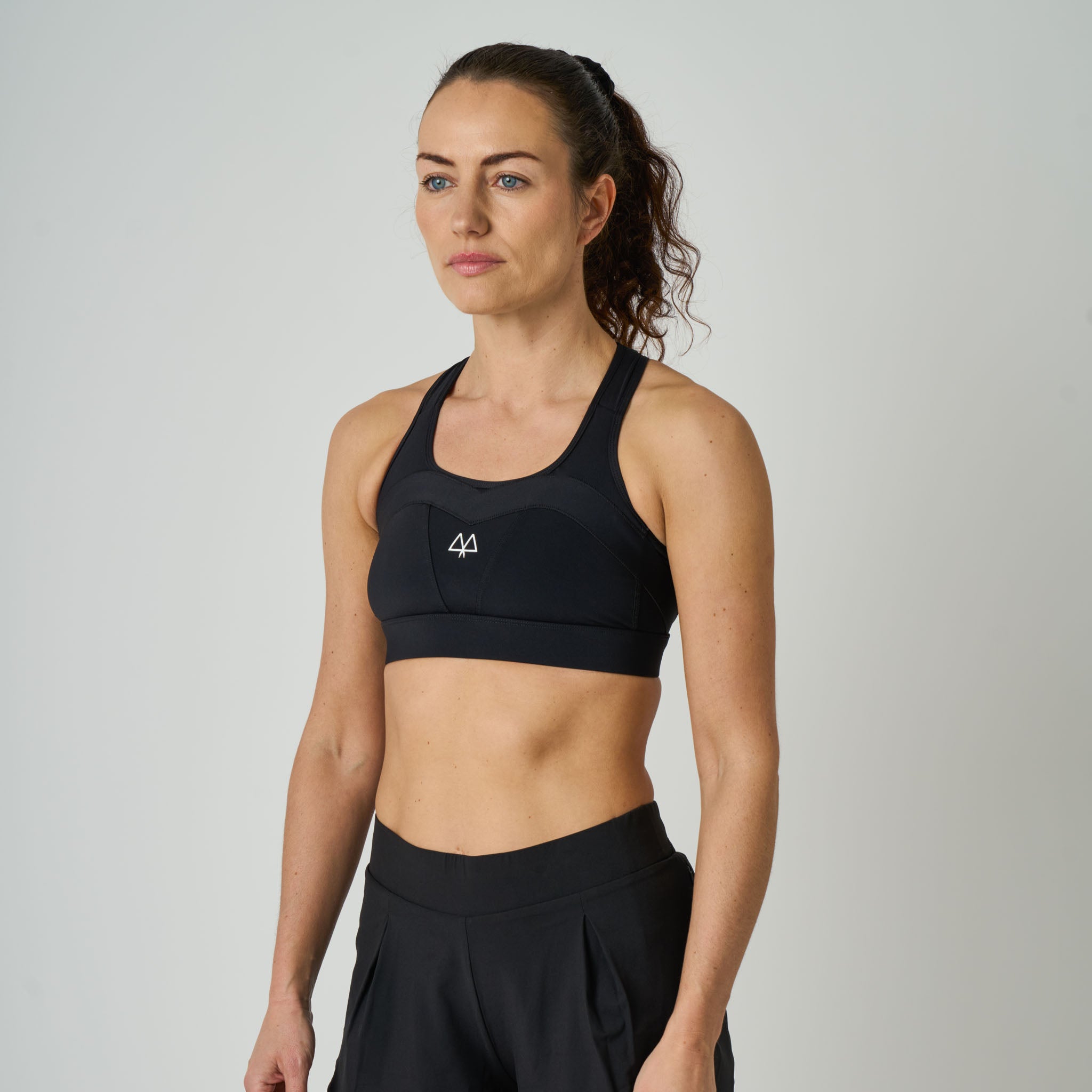 Woman wearing a black sports bra with a logo on a plain background