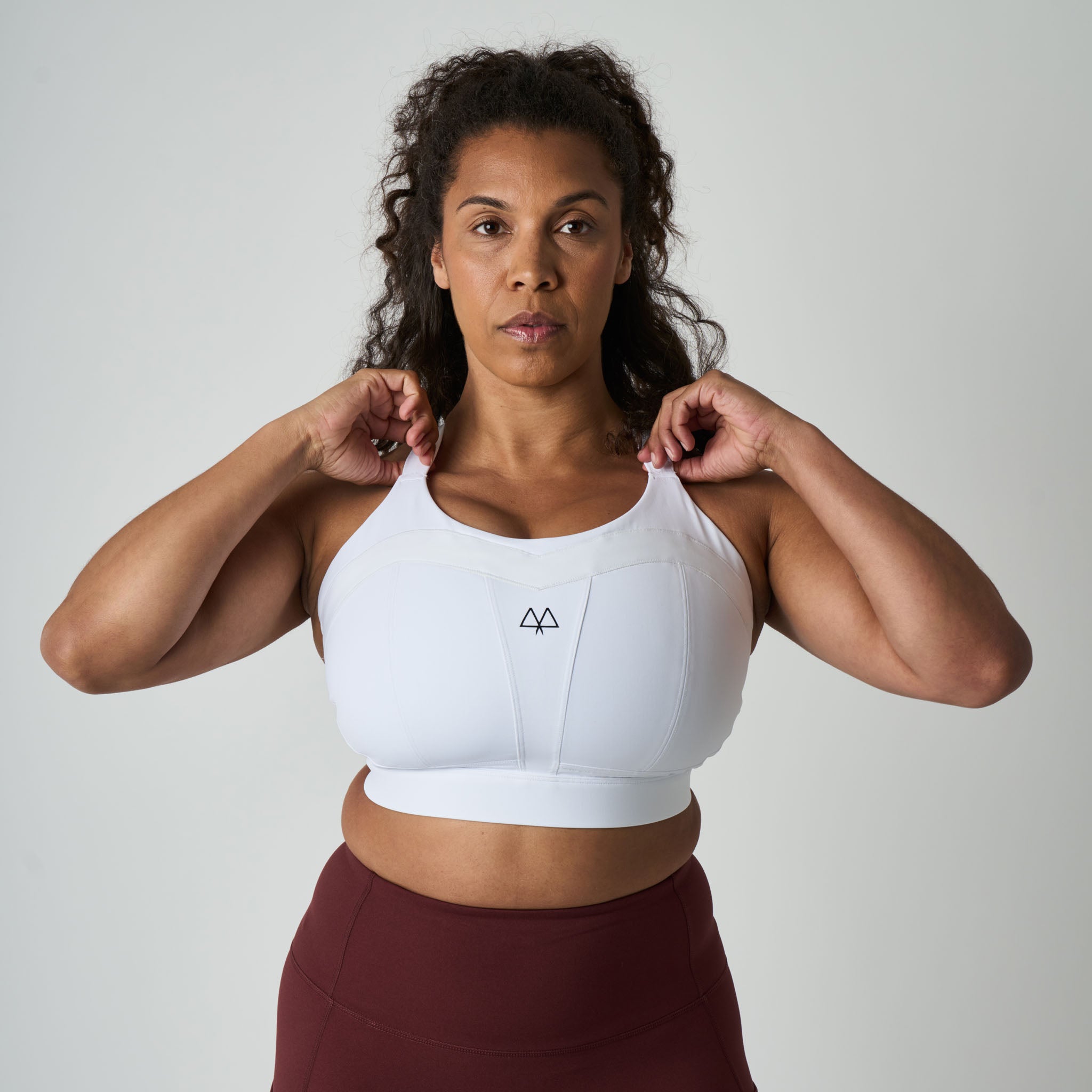 Woman wearing a white sports bra with a logo on a plain background