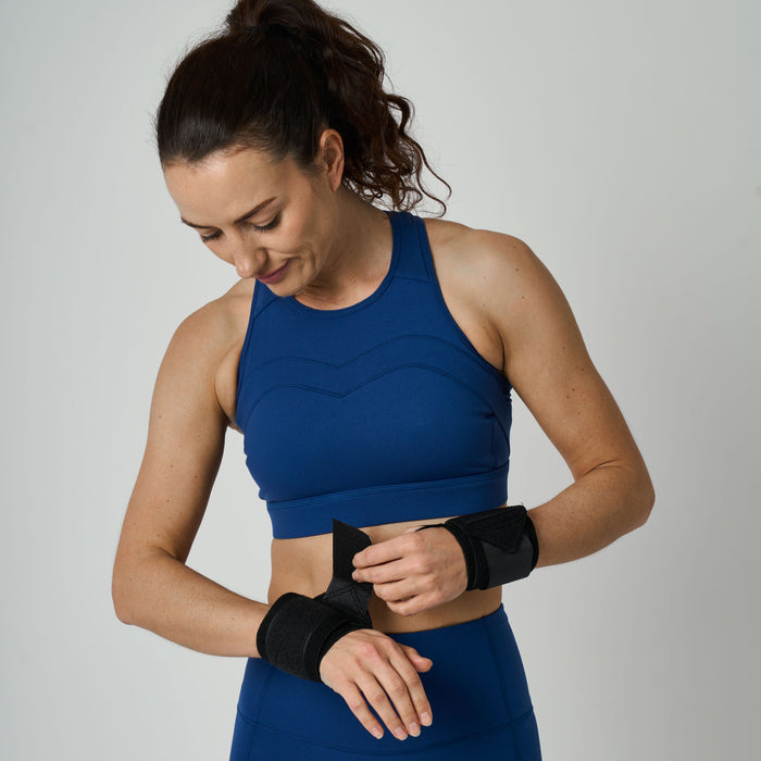 Woman in blue athletic wear with black wrist wraps on a plain background