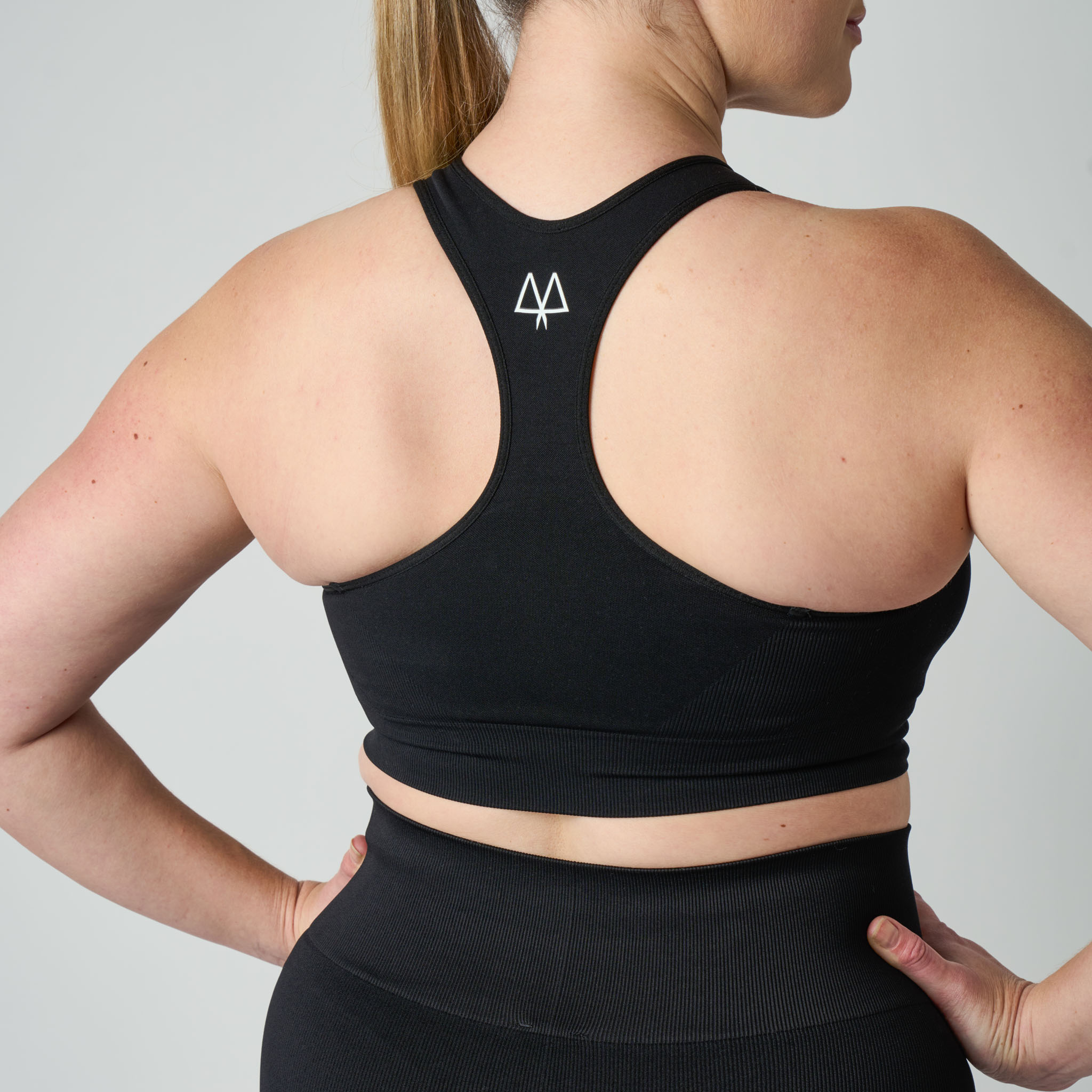 Person wearing a black sports bra with a logo on the back against a gray background