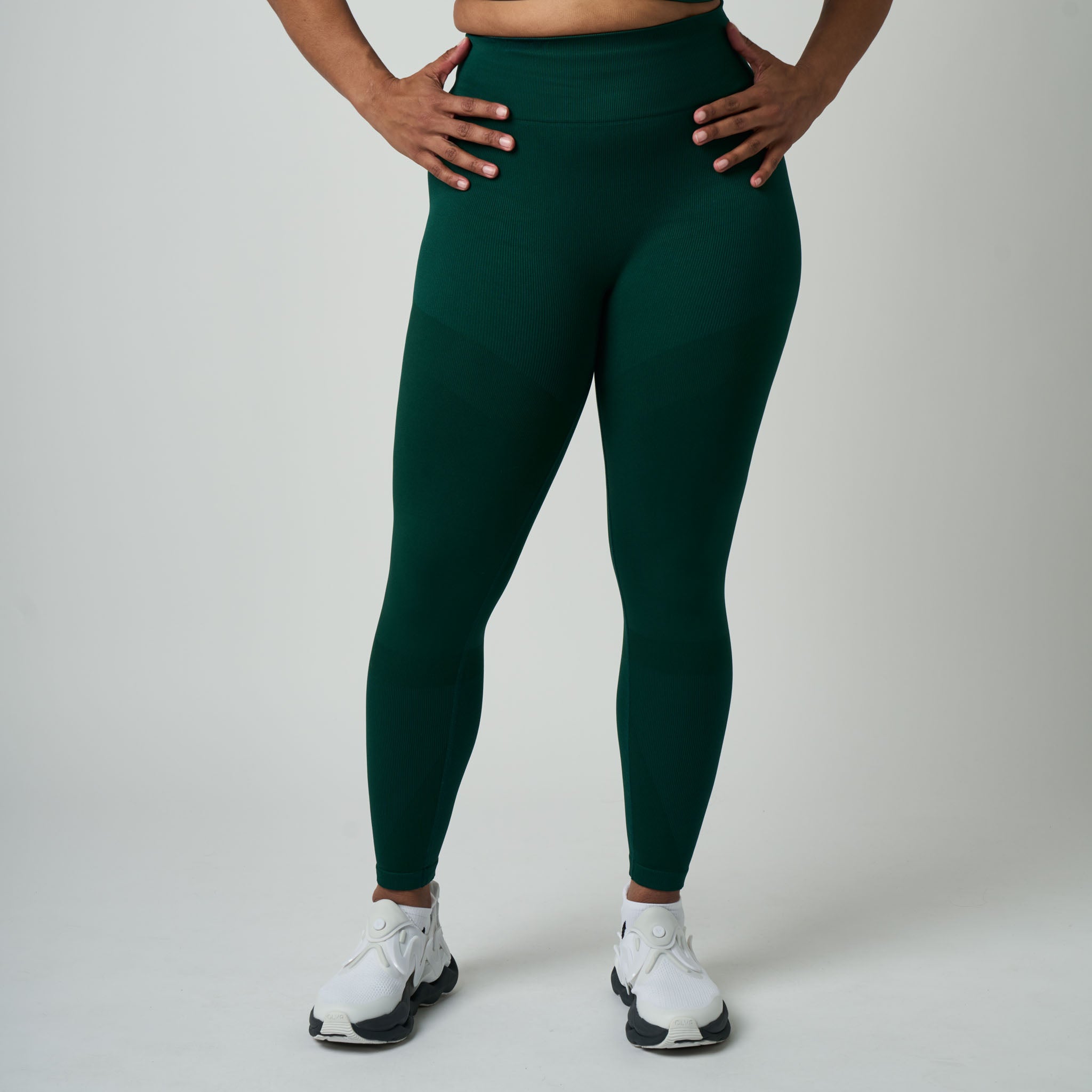 Person wearing dark green leggings and white sneakers on a plain background
