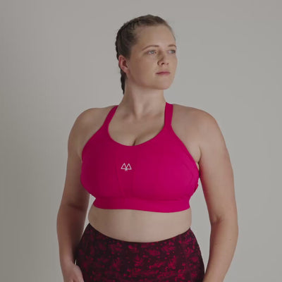 Woman wearing a pink sports bra and maroon patterned leggings on a gray background