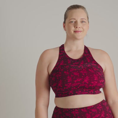 Person wearing a red and black patterned sports bra and leggings on a plain background
